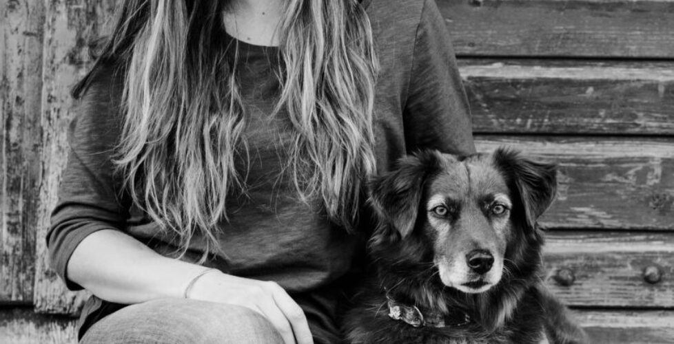 Die Hundefotografin sitzt gemeinsam mit ihrem Hund Finn vor einer Hütte