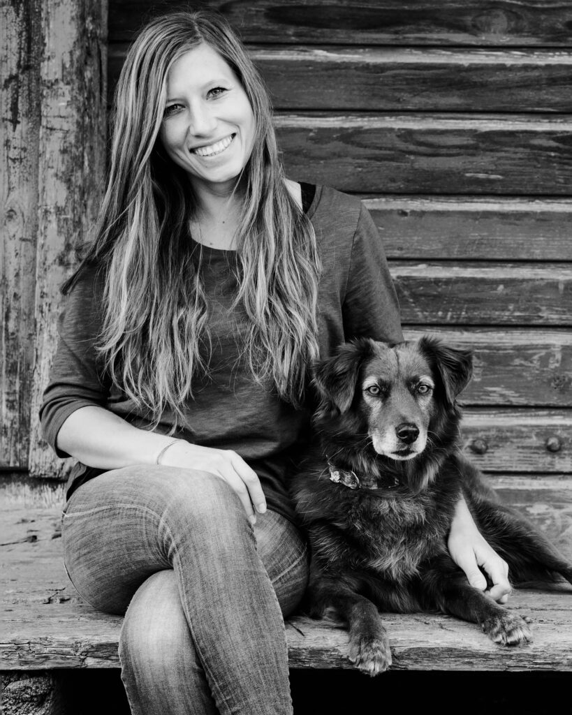 Die Hundefotografin sitzt gemeinsam mit ihrem Hund Finn vor einer Hütte